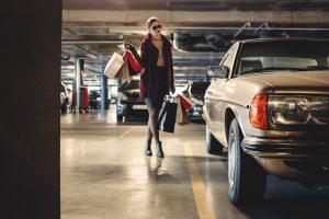woman carrying shopping paper bags walking towards beige car inside parking lot
